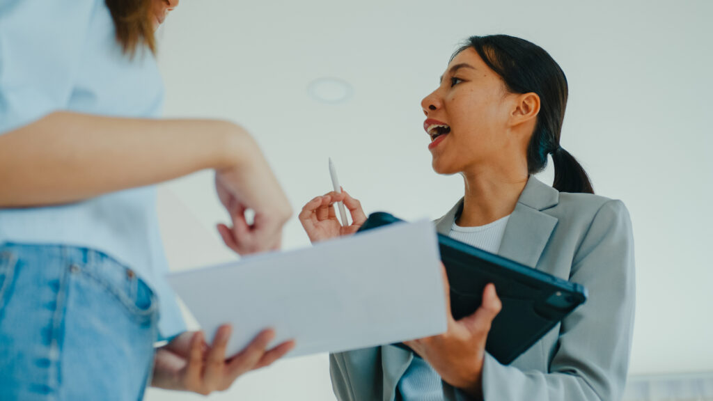 Close-up of Asian female real estate agent explaining and showing living room in new house to tenants for rent or buy. Landlord selling real estate to happiness couple customer.